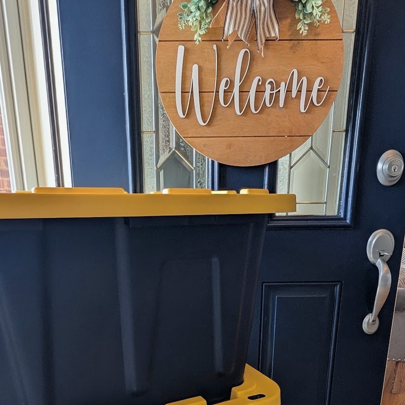 A stack of Crate & Key moving totes delivered on a front porch beside a navy front door with a Welcome sign